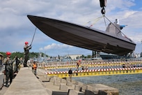 Lt. Jay Faylo, unmanned systems director of Commander Task Force 66 (CTF-66), directs the crane operator lowering a K3 Scout, an unmanned surface vessel, into the Port of Gdynia for acceptance and validation of the craft and capabilities development for project Vesuvius during exercise Baltic Operations (BALTOPS) 2026, June 12, 2026.