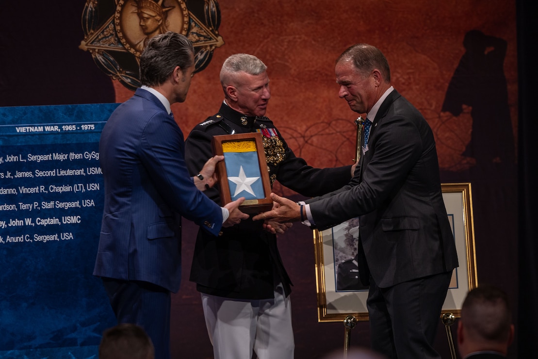 Secretary of War Pete Hegseth, left, and the 39th Commandant of the Marine Corps, Gen. Eric M. Smith, center, present a Medal of Honor flag to Mr. Thomas Ripley on behalf of his father, U.S. Marine Corps Col. John Ripley, during the Hall of Heroes Induction Ceremony at Arlington, Virginia, June 19, 2026. Maj. Capers and Col. Ripley received the nation’s highest military decoration for extraordinary heroism and conspicuous gallantry during the Vietnam War. (U.S Marine Corps photo by Lance Cpl. Aiyana Bridges)