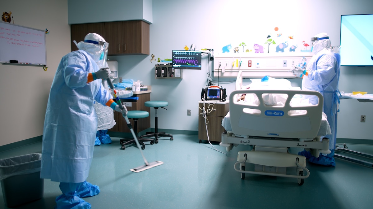 A medical professional from the Center for Sustainment of Trauma and Readiness Skills (C-STARS) Omaha, in full personal protective equipment, mops the floor while another team member tends to a simulated patient at the University of Nebraska Medical Center, June 14, 2024.