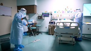 A medical professional from the Center for Sustainment of Trauma and Readiness Skills (C-STARS) Omaha, in full personal protective equipment, mops the floor while another team member tends to a simulated patient at the University of Nebraska Medical Center, June 14, 2024.