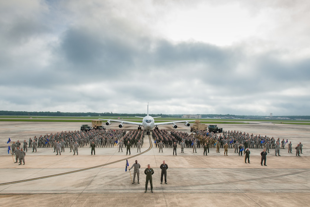 A group of military personnel pose for a photo with an airplane in the background