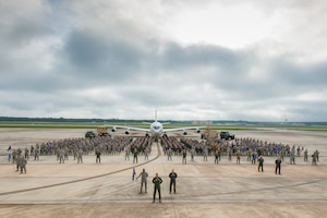A group of military personnel pose for a photo with an airplane in the background