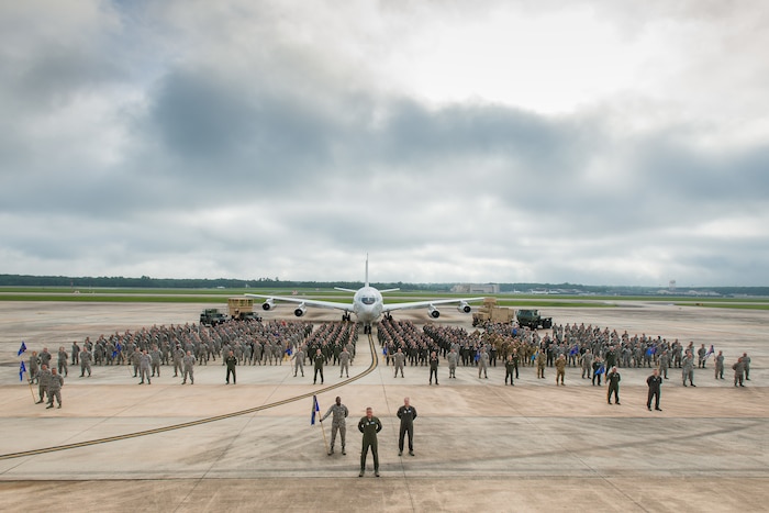 A group of military personnel pose for a photo with an airplane in the background