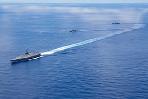 Three large military ships sail in the ocean.
