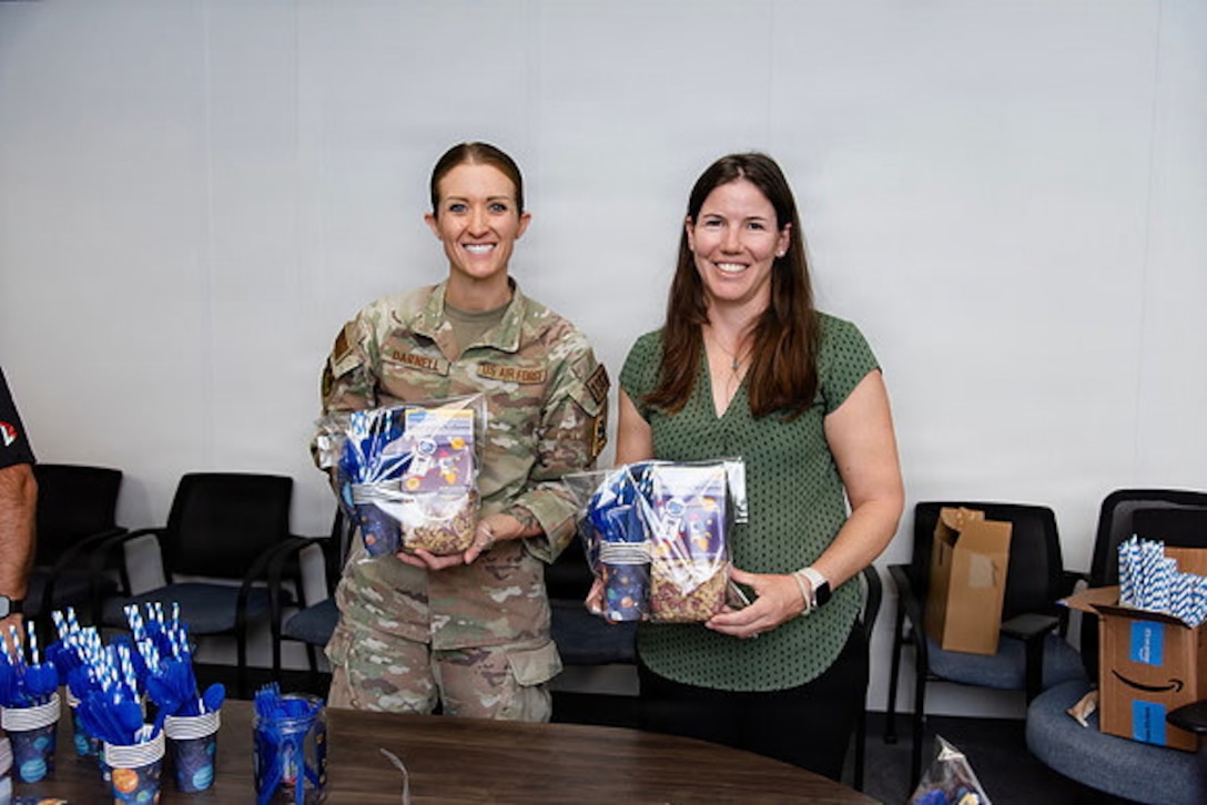 Guardians and volunteers pack boxes of gifts in a room for family members of deployed Guardians. Everyone is either in uniform or civilian clothes and they're in an office/conference space