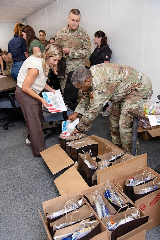 Guardians and volunteers pack boxes of gifts in a room for family members of deployed Guardians. Everyone is either in uniform or civilian clothes and they're in an office/conference space