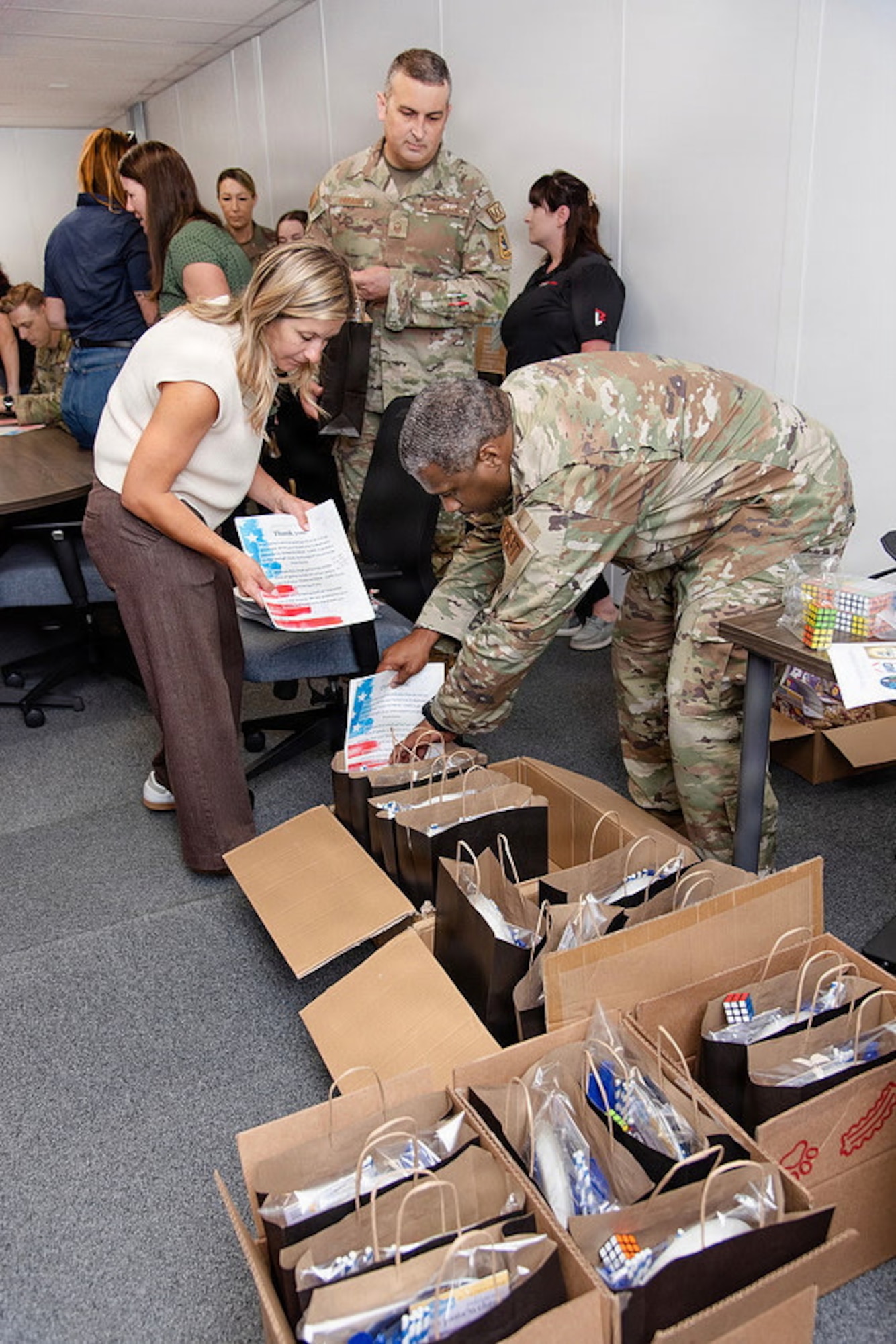 Guardians and volunteers pack boxes of gifts in a room for family members of deployed Guardians. Everyone is either in uniform or civilian clothes and they're in an office/conference space