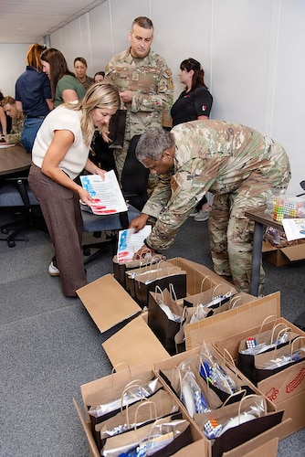 Guardians and volunteers pack boxes of gifts in a room for family members of deployed Guardians. Everyone is either in uniform or civilian clothes and they're in an office/conference space