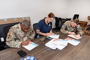 Guardians and volunteers pack boxes of gifts in a room for family members of deployed Guardians. Everyone is either in uniform or civilian clothes and they're in an office/conference space