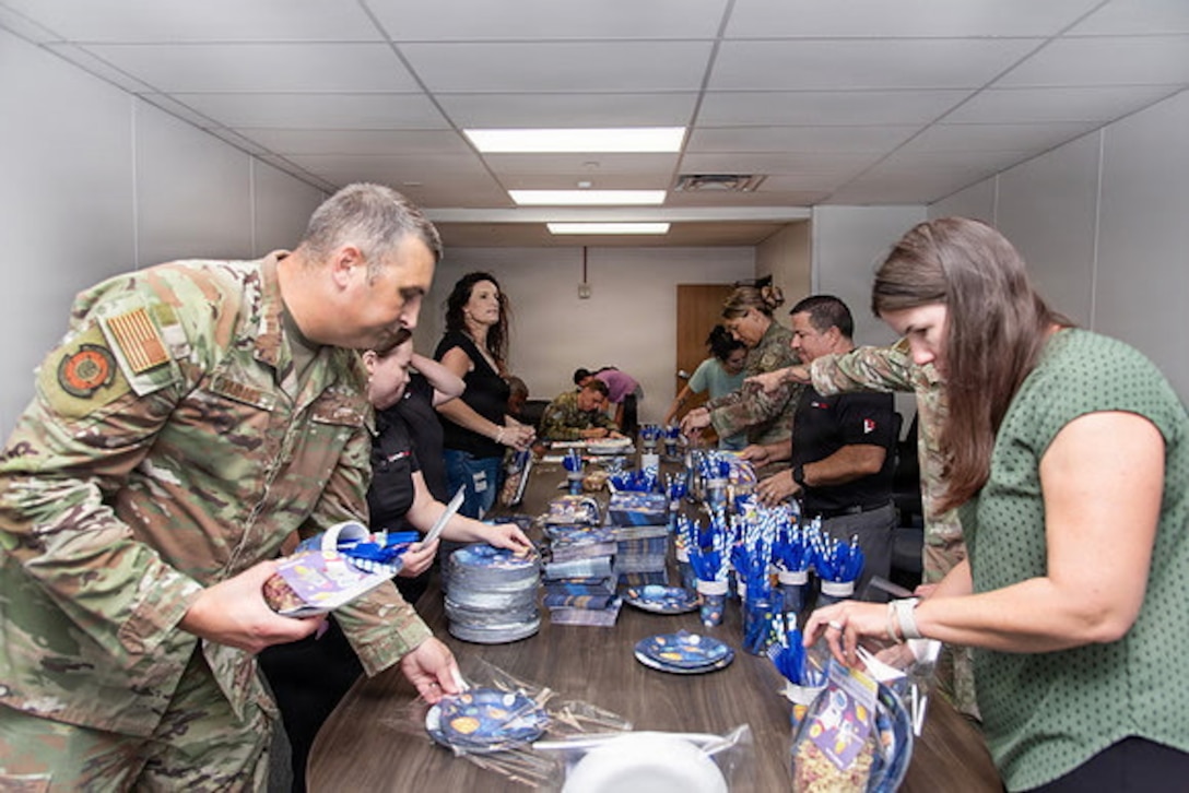 Guardians and volunteers pack boxes of gifts in a room for family members of deployed Guardians. Everyone is either in uniform or civilian clothes and they're in an office/conference space