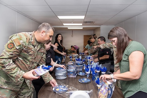 Guardians and volunteers pack boxes of gifts in a room for family members of deployed Guardians. Everyone is either in uniform or civilian clothes and they're in an office/conference space