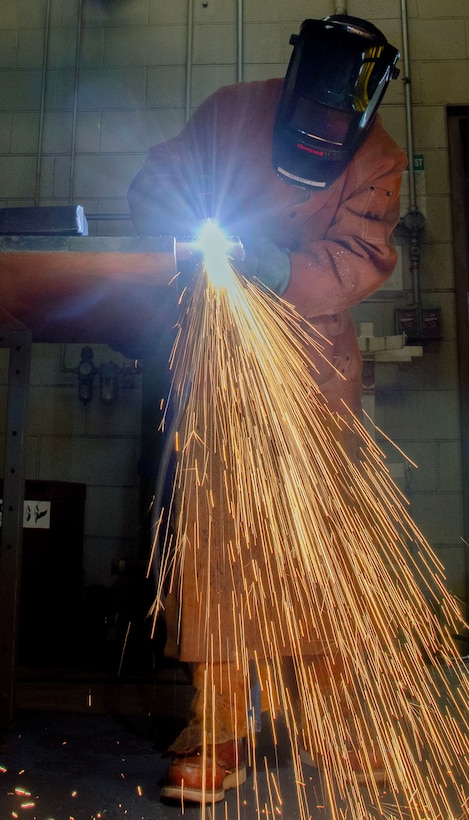 A person in PPE cuts metal with lots of sparks falling to the floor