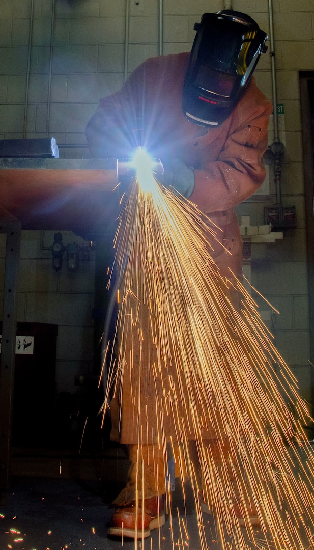 A person in PPE cuts metal with lots of sparks falling to the floor