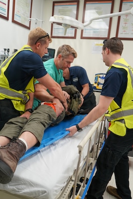 Hospital Corpsman 2nd Class John Paul Manikas and Hospital Corpsman 3rd Class Michael Blanchard, assigned to Naval Medical Readiness and Training Command (NMRTC) Rota, assist with transferring a simulated casualty in the Emergency Department alongside Lt. Cmdr. Matthew Britt during an Air Mishap exercise at Naval Station Rota, May 20, 2026. The exercise provided medical personnel an opportunity to practice patient movement, emergency care procedures, and coordination between prehospital and hospital teams in a realistic training environment. The training enhanced coordination among responding agencies and strengthened the readiness of Navy Medicine personnel to provide lifesaving care and medical support during operational, contingency, and emergency response missions. (U.S. Navy photo by Lt. Vanessa Bernales)