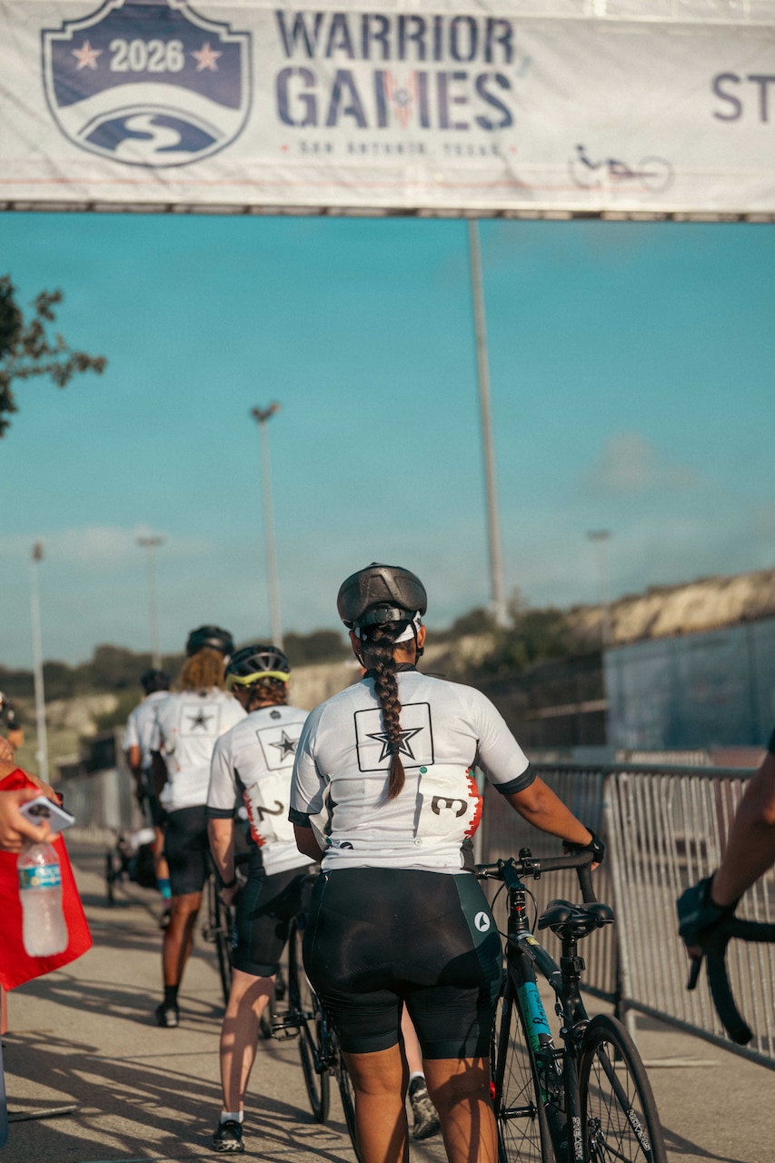 People wearing sports gear and helmets push their bikes to the starting line of a race.