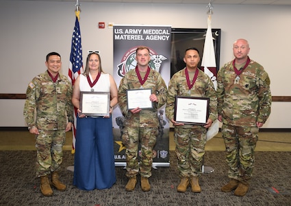 From left: USAMMA Commander Col. Joselito Lim, Kellie Pugh, Maj. Jeremy Searles, Master Sgt. Ceasar Juan, and Sgt. Maj. Todd Brenecki pose for a group photo at Fort Detrick, Md. Pugh, Searles, and Juan hold framed certificates and wear Order of Military Medical Merit, or O2M3, medallions following their induction into the prestigious organization.