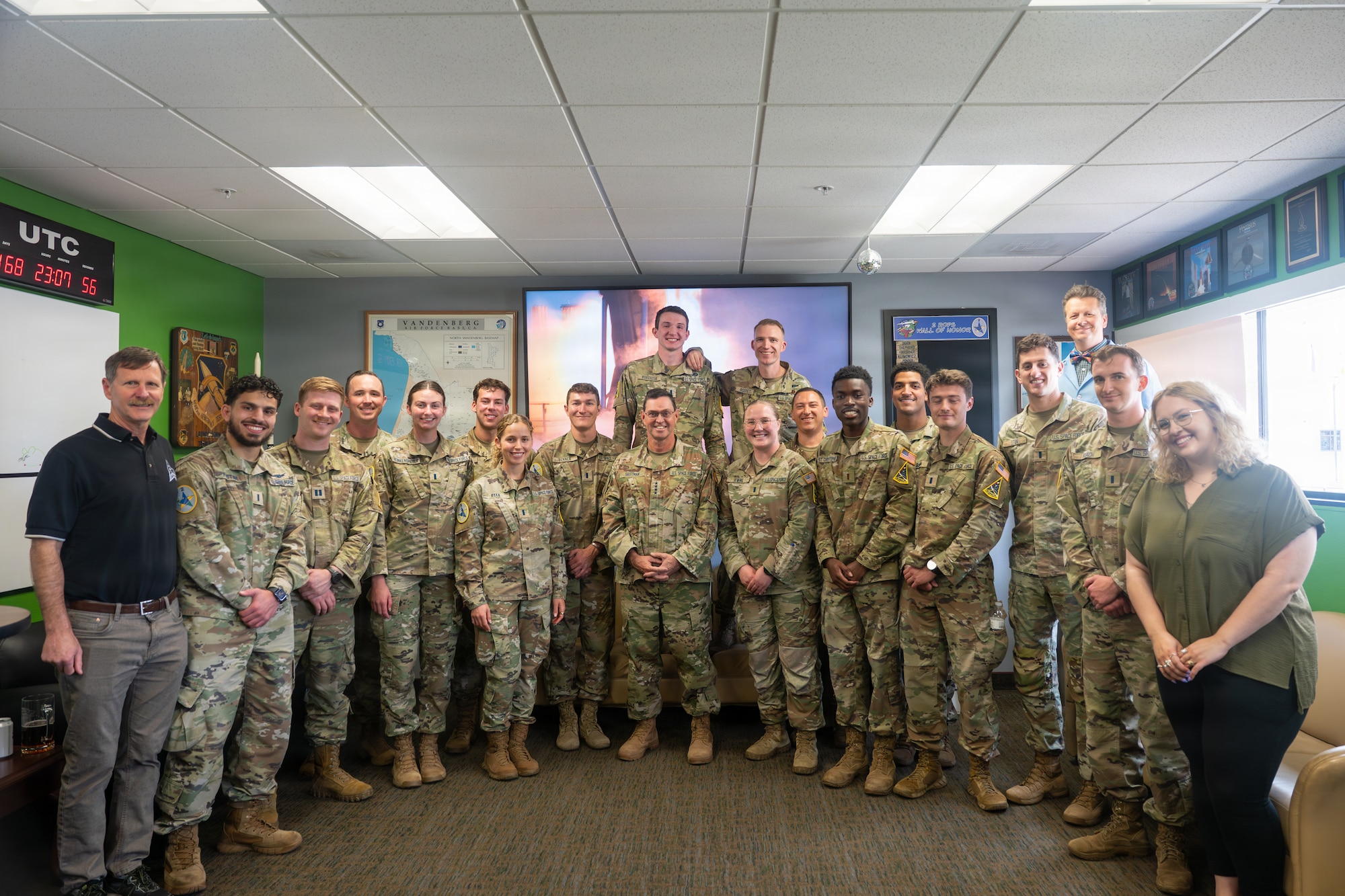 The 2nd Range Operations Squadron pose with the general in their heritage room as a screen plays launches in the background.