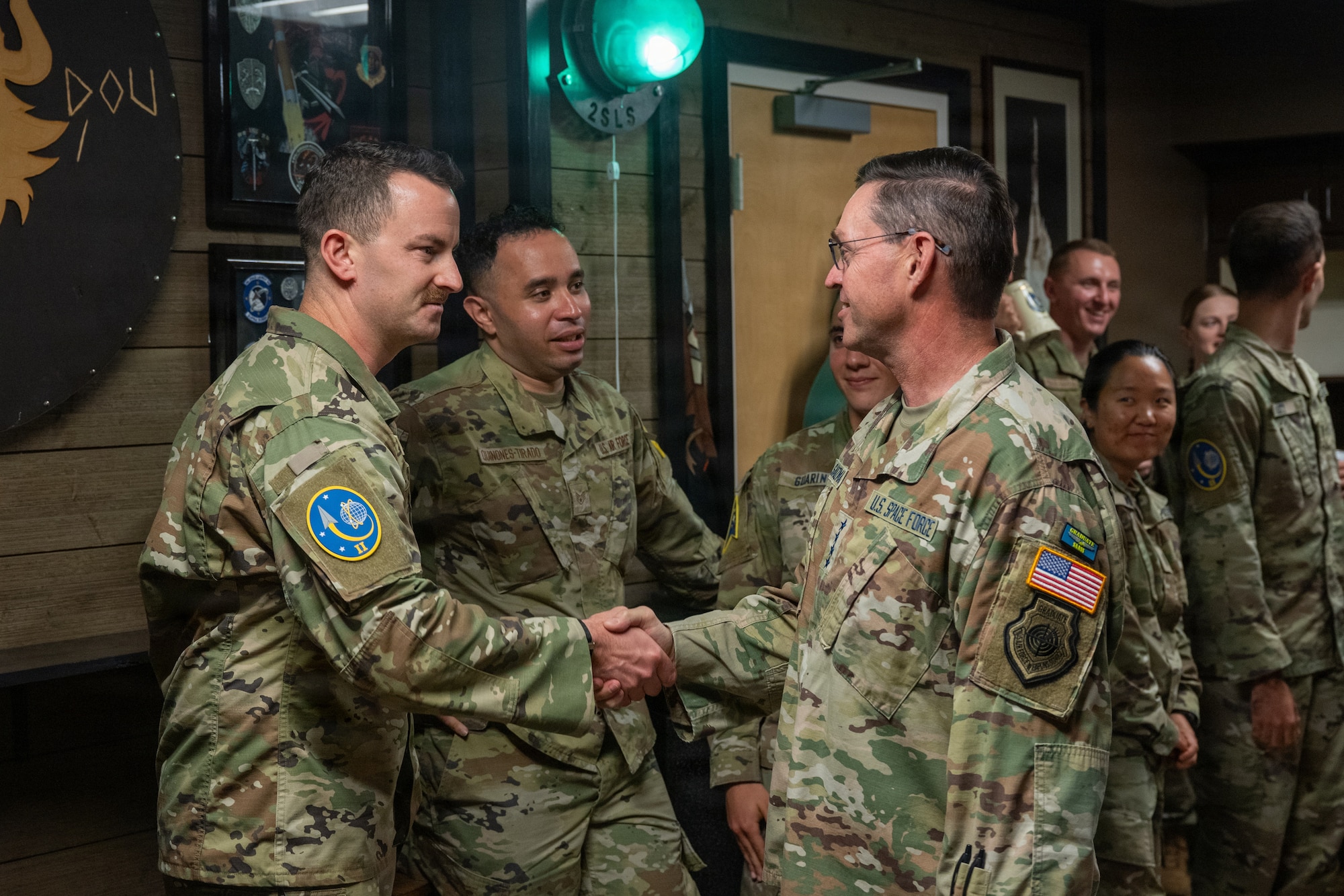 The general shakes hands with a lieutenant in a Viking style heritage room filled with Space Force military members and civilians.
