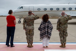 Two Space Force Officers salute the jet carrying the Chief of Space Operations, while accompanied by their wives
