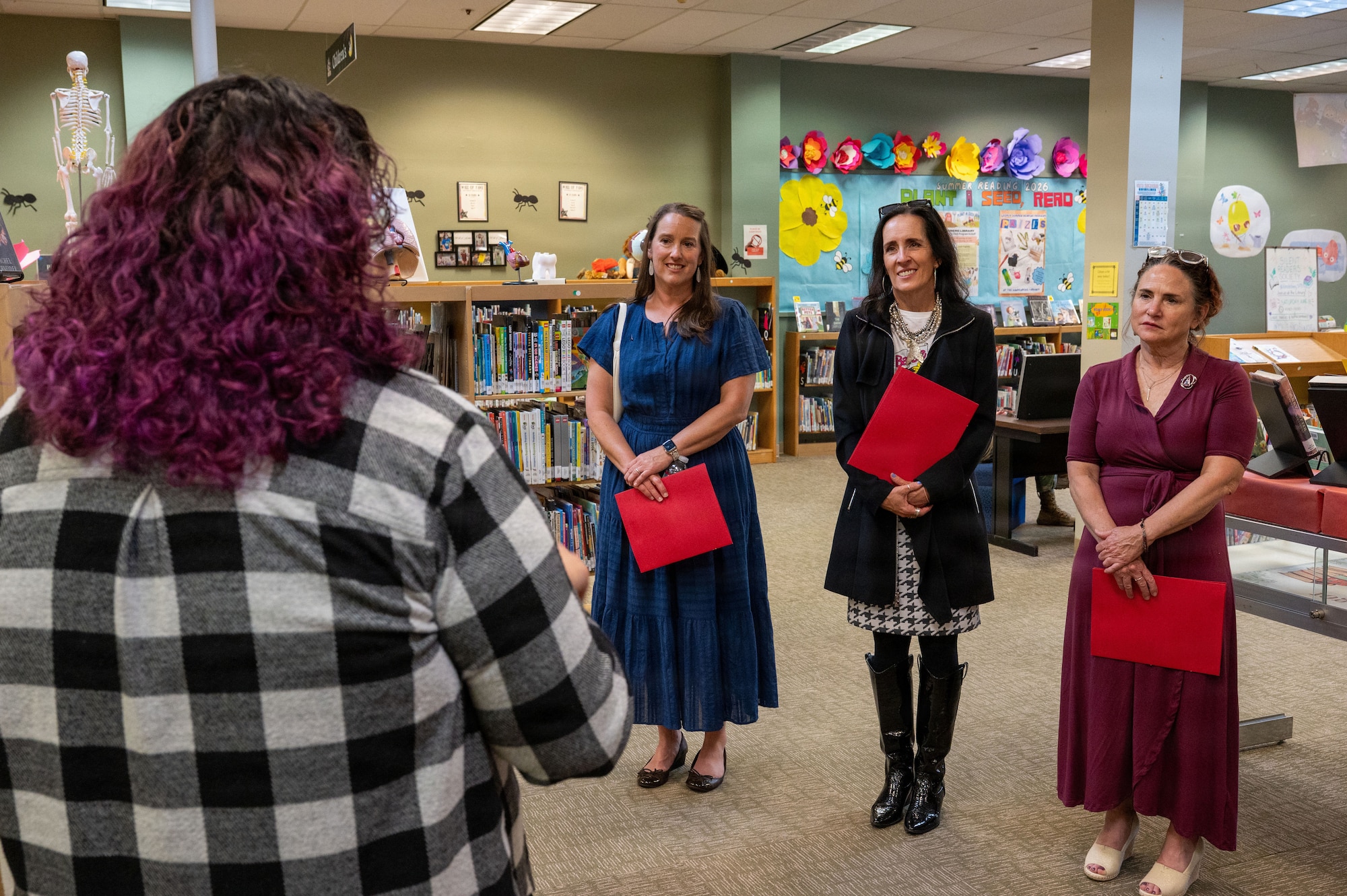 A woman is speaking to a trio of women in a library.