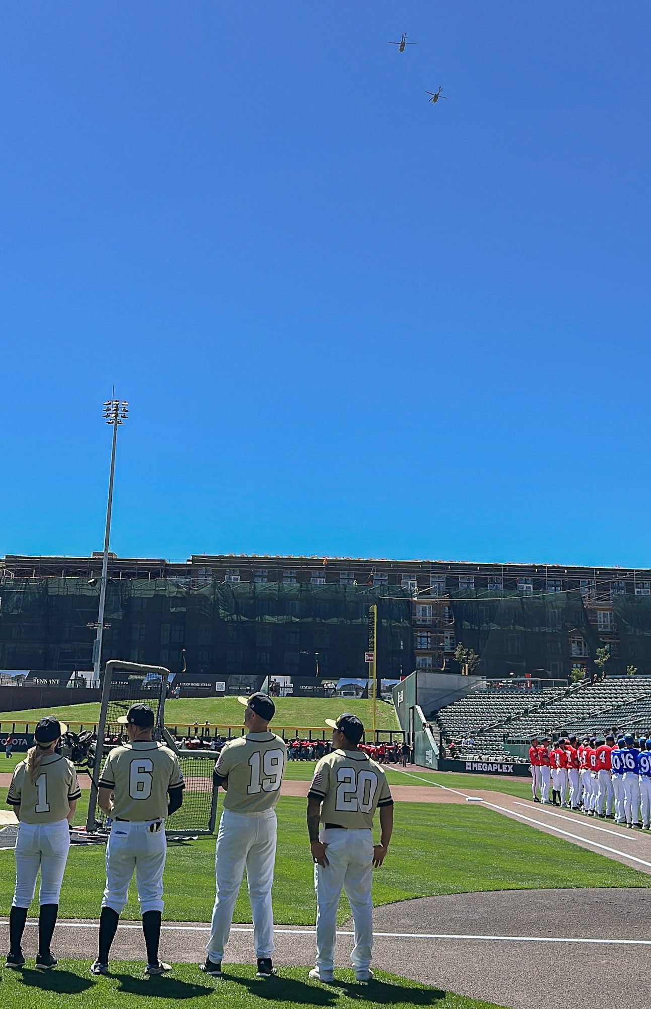 Utah National Guard and Hill Air Force Base players stand along the first-base line as helicopters fly over The Ballpark at America First Square before an exhibition baseball game in South Jordan, Utah, June 13, 2025. The game followed the "In the Open: Strength Beyond the Uniform" resilience event, which focused on mental health awareness, resilience and community support. (Utah National Guard photo by Master Sgt. Nicholas Perez)