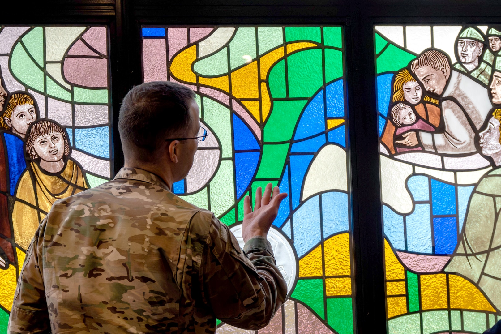 An airman wearing a camouflage uniform looks at a stained glass window.