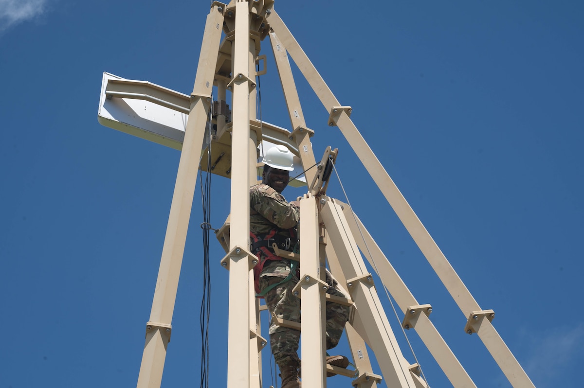 an airman smiles down while suspended atop a glide slope antenna