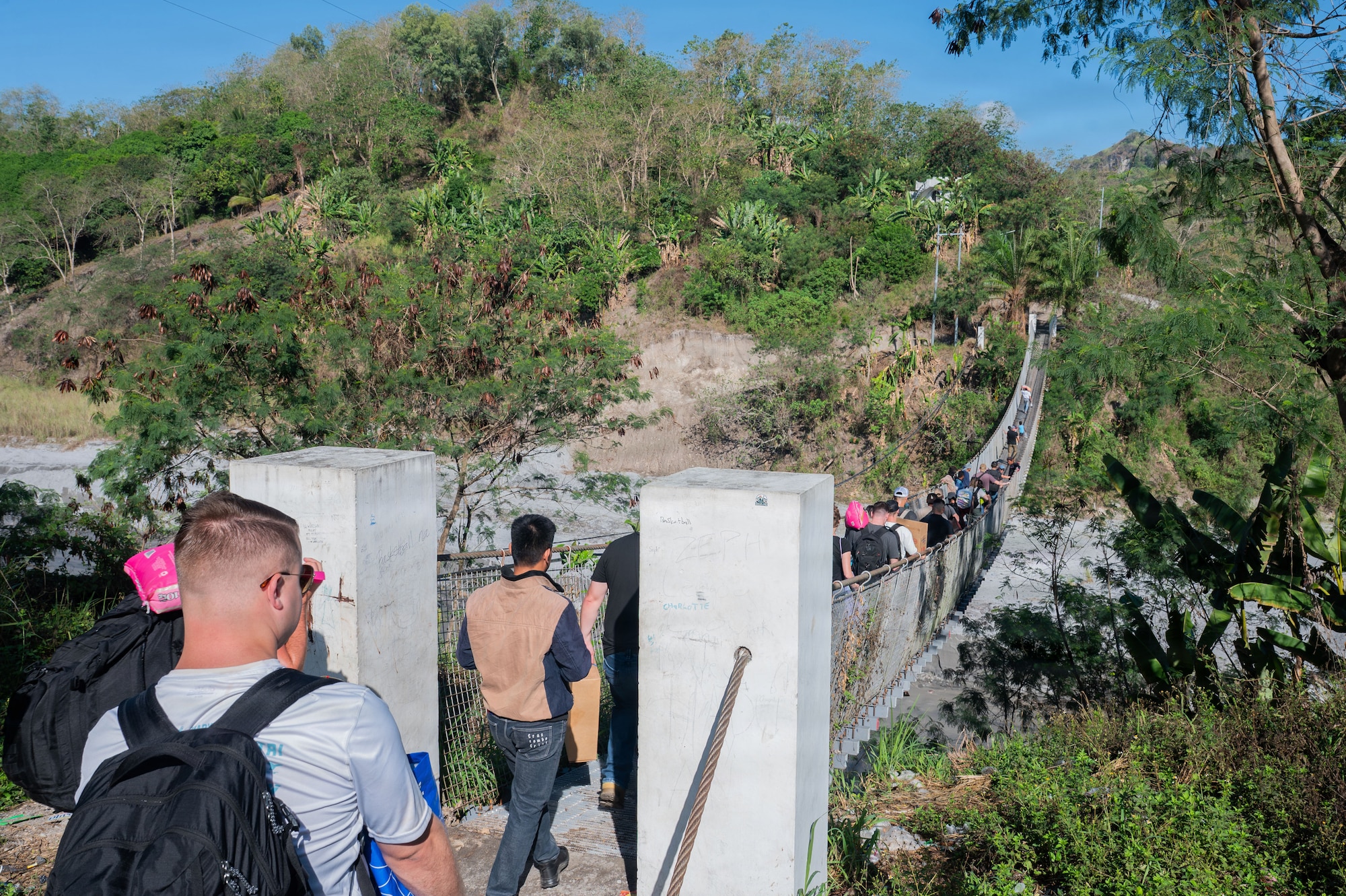 U.S. Airmen assigned to the 21st Air Expeditionary Wing cross a bridge on their way to Haduan Village during a humanitarian outreach event in the Philippines, May 20, 2026. Airmen hiked to the village to deliver school supplies and engage with local children, fostering goodwill and building trust within the local community. (U.S. Air Force photo by Senior Airman Alondra Cristobal Hernandez)