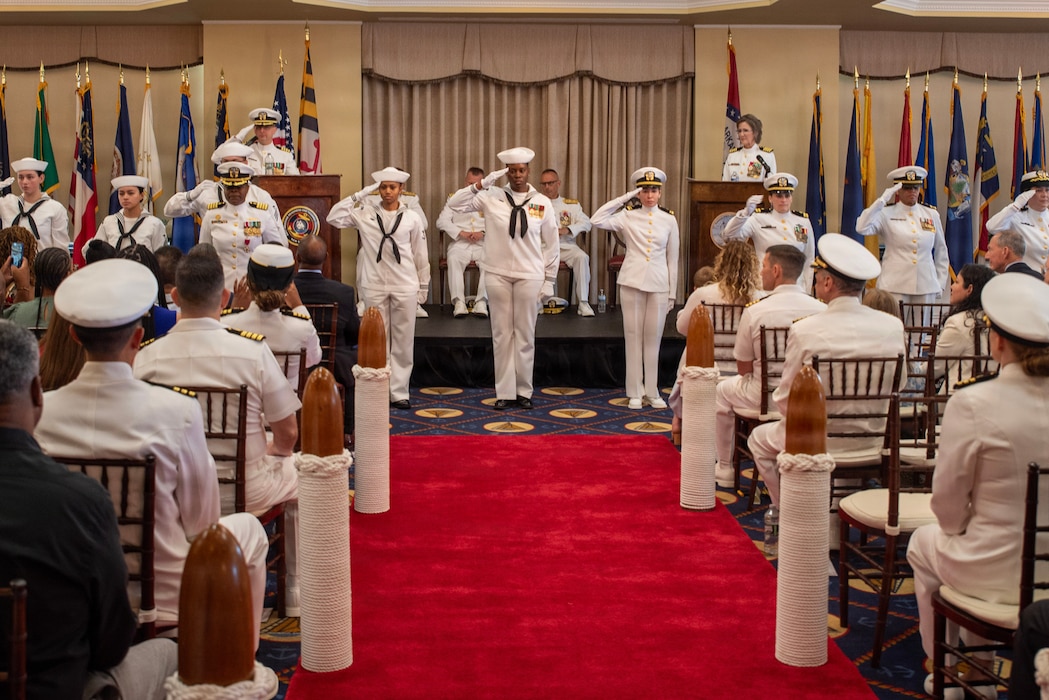 Capt. Rona Green, outgoing commanding officer of Navy Medicine Readiness and Training Command New England, presents a folded ensign to her husband, following a flag passing ceremony during her retirement ceremony aboard Naval Station Newport, R.I., June 10, 2026. Green served the Navy for 37 years of dedicated and honorable service. (U.S. Navy photo by Mass Communication Specialist 1st Class Jacob Allison)