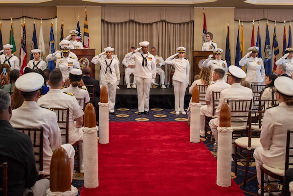Capt. Rona Green, outgoing commanding officer of Navy Medicine Readiness and Training Command New England, presents a folded ensign to her husband, following a flag passing ceremony during her retirement ceremony aboard Naval Station Newport, R.I., June 10, 2026. Green served the Navy for 37 years of dedicated and honorable service. (U.S. Navy photo by Mass Communication Specialist 1st Class Jacob Allison)
