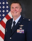 photo of USAF Airman in service dress standing in front of the US flag