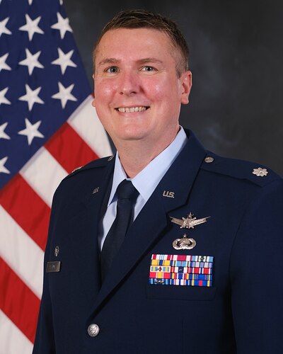 photo of USAF Airman in service dress standing in front of the US flag