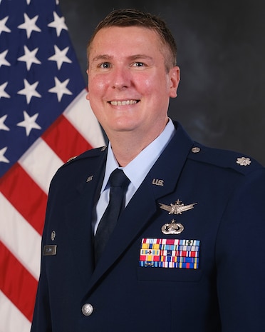 photo of USAF Airman in service dress standing in front of the US flag