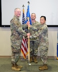 photo of three USAF Airmen standing on a stage, two Airmen are holding a unit flag in between them