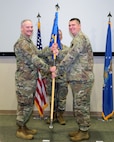 photo of three USAF Airmen standing on a stage, two Airmen are holding a unit flag in between them