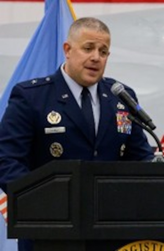 Air force one-star general standing at a podium during a ceremony delivering remarks to attendees seated in the audience.