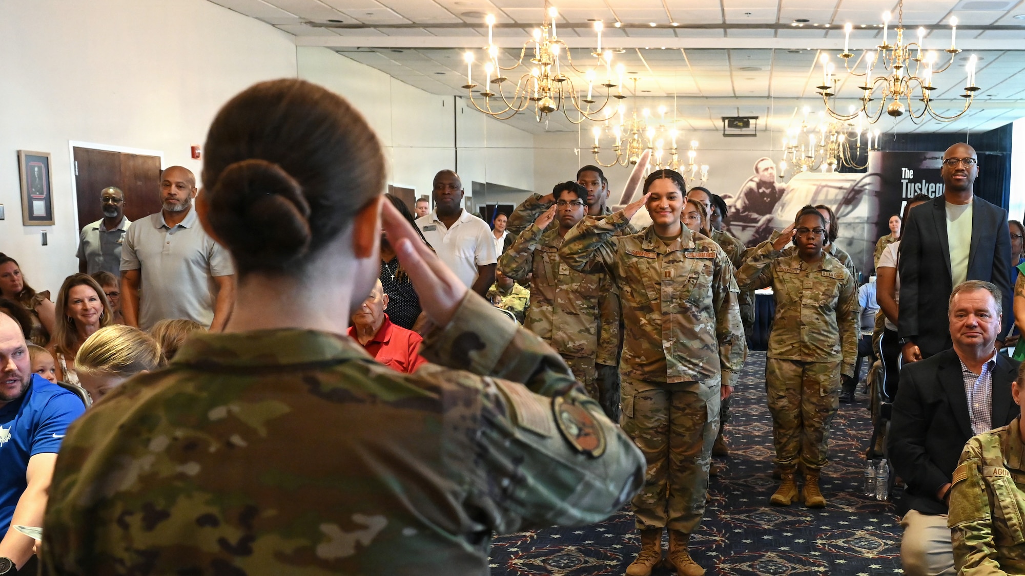 Photo of an Air Force squadron commander in the foreground saluting a formation of Airmen in the background inside a ballroom club.