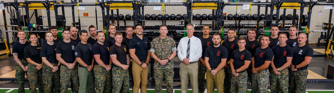 Nicholas Gounaris, the director of strength and conditioning with Warrior Athlete Readiness and Resilience, center left, U.S. Marine Corps Col. Robert McCarthy III, the commanding officer of The Basic School, center, and Brad Brimhall, the branch head with Warrior Athlete Readiness and Resilience, center right, pose for a group photo with the Martial Arts Fitness and Center of Excellence staff at Ramer Hall on Marine Corps Base Quantico, Virginia, June 16, 2026. The Ramer Hall facility upgrades strengthen the vital partnerships between TBS, Basic Officer Course, MAFCE and other units. This collaboration establishes a sustainable foundation for optimizing human performance and resiliency across the entire Marine Corps. (U.S. Marine Corps photo by Lance Cpl. Lynsee Avila-Ramirez)