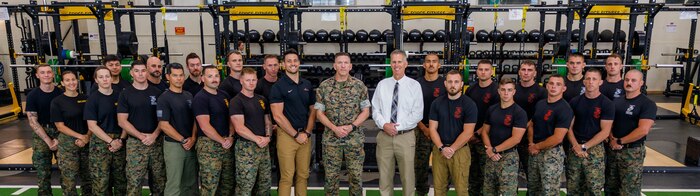 Nicholas Gounaris, the director of strength and conditioning with Warrior Athlete Readiness and Resilience, center left, U.S. Marine Corps Col. Robert McCarthy III, the commanding officer of The Basic School, center, and Brad Brimhall, the branch head with Warrior Athlete Readiness and Resilience, center right, pose for a group photo with the Martial Arts Fitness and Center of Excellence staff at Ramer Hall on Marine Corps Base Quantico, Virginia, June 16, 2026. The Ramer Hall facility upgrades strengthen the vital partnerships between TBS, Basic Officer Course, MAFCE and other units. This collaboration establishes a sustainable foundation for optimizing human performance and resiliency across the entire Marine Corps. (U.S. Marine Corps photo by Lance Cpl. Lynsee Avila-Ramirez)