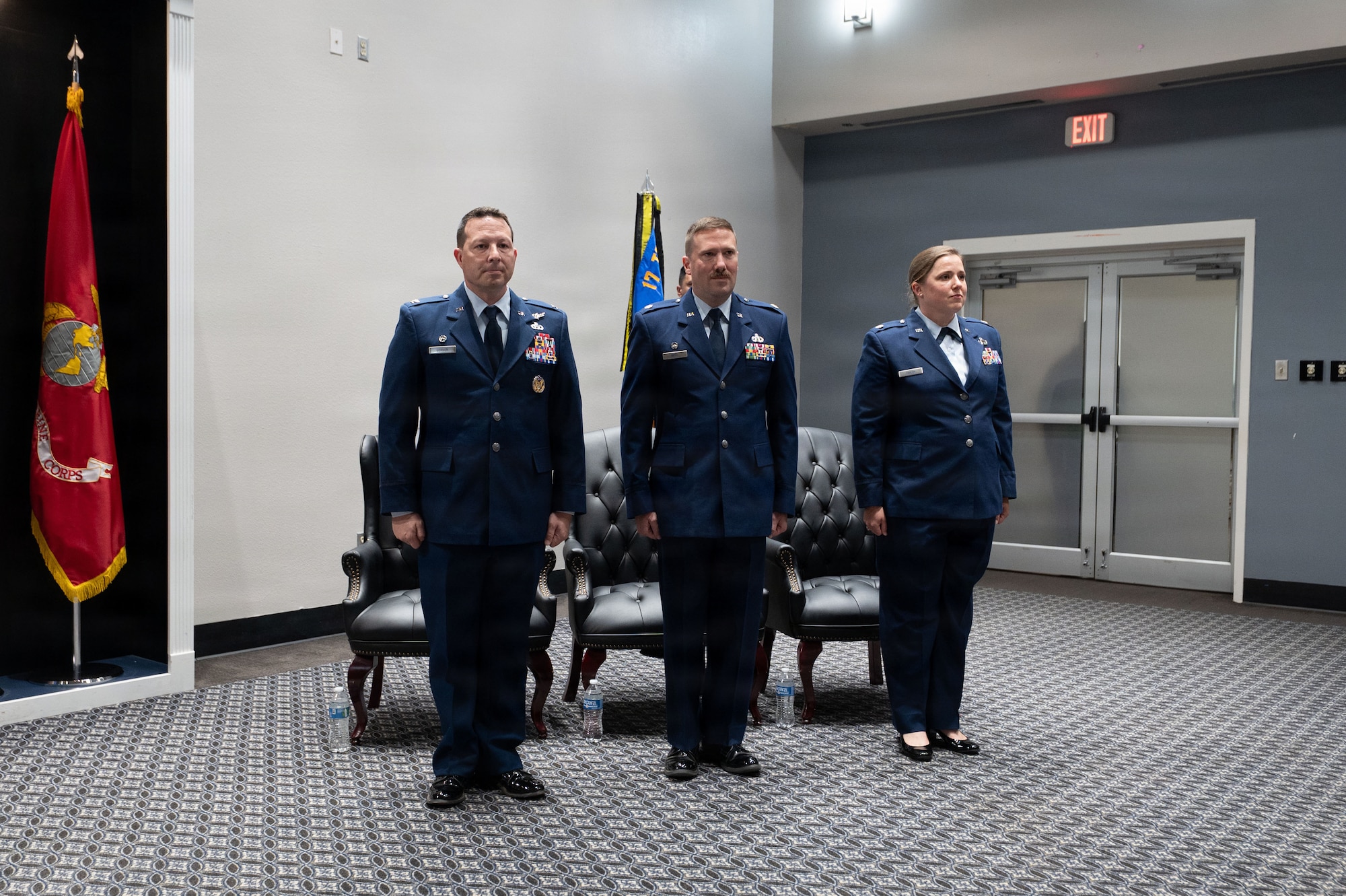 Three service members stand at attention in service dress