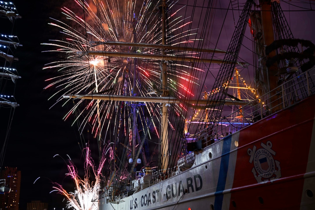Red, white and blue fireworks illuminate a night sky over a partially visible Coast Guard ship.