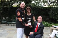 From left, Sgt. Maj. of the Marine Corps and Evening Parade host, Micheal P. Barrett; Rosemarie Cooper; and the Parade guest of honor, Dr. Rory Cooper, pose for a photo following a gift exchange during the Parade reception at Marine Barracks Washington in Washington, D.C.