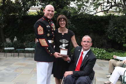 From left, Sgt. Maj. of the Marine Corps and Evening Parade host, Micheal P. Barrett; Rosemarie Cooper; and the Parade guest of honor, Dr. Rory Cooper, pose for a photo following a gift exchange during the Parade reception at Marine Barracks Washington in Washington, D.C.