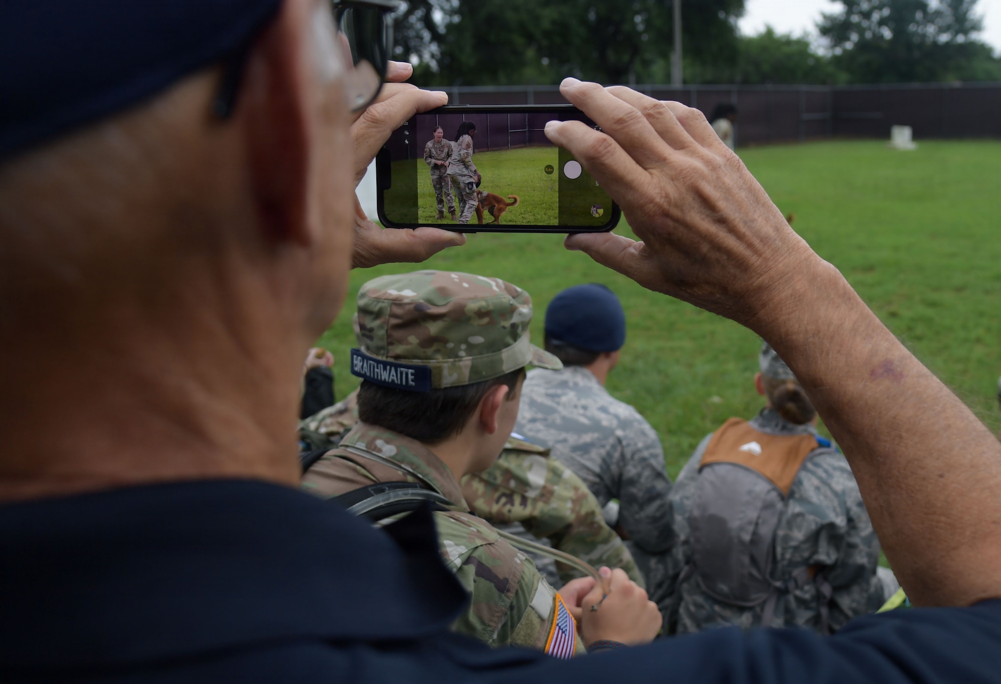 A man holds a phone as it records a military working dog demonstration.