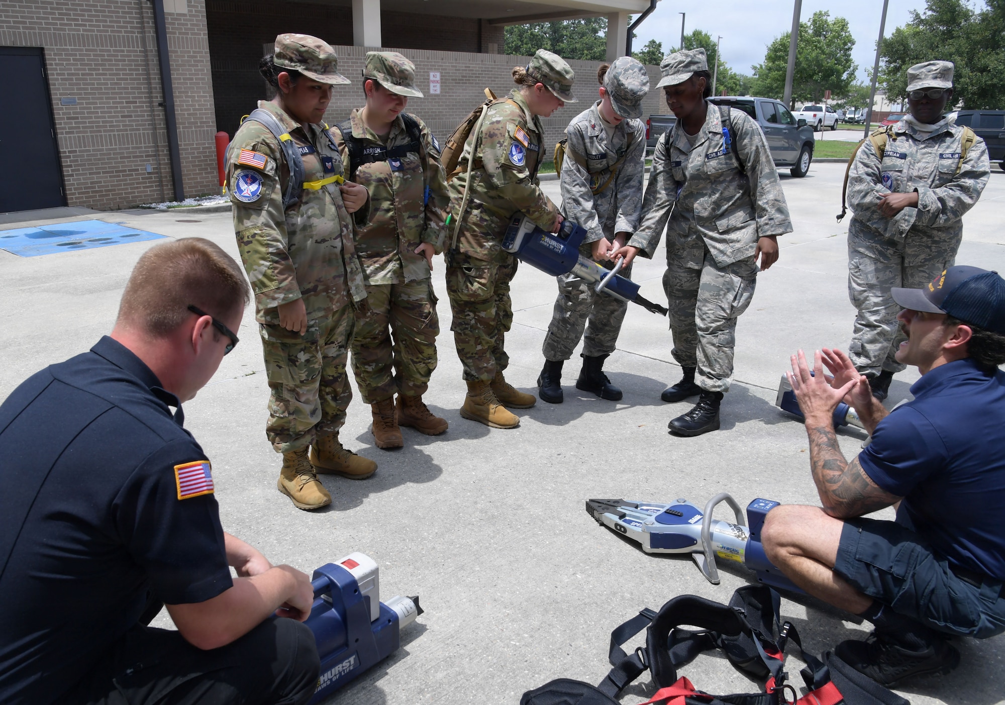 Two firefighters speak to a group of civil air patrol cadets while holding jaws of life equipment.