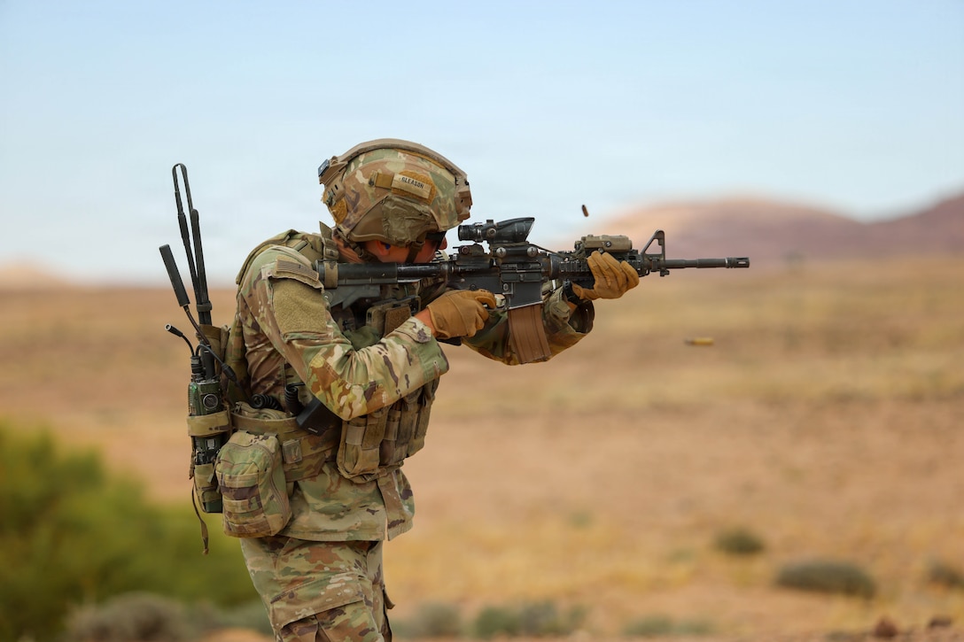 A soldier fires a military rifle in the desert, and shell casings fly out of the weapon.