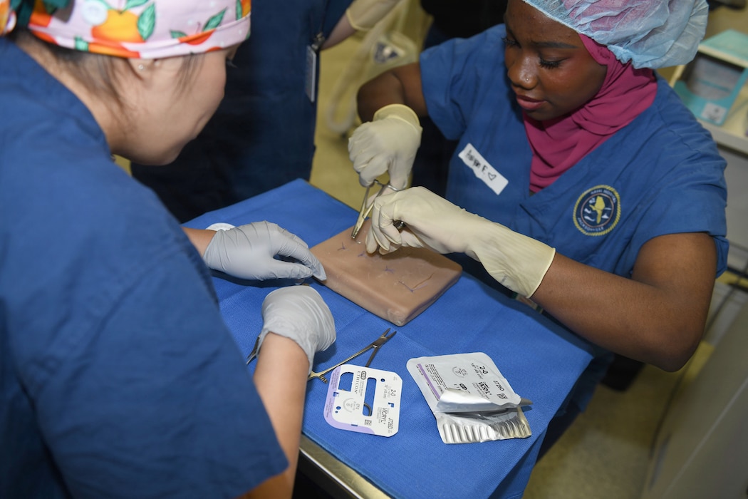260610-N-JB216-5830 Jacksonville, Fla. (June 12, 2026) The annual Science, Service, Medicine, and Mentoring (S2M2) program at Naval Hospital Jacksonville concluded another impactful week!  From June 8-12, students from Darnell-Cookman School of the Medical Arts explored a variety of medical departments, gaining firsthand experience through hands-on activities, demonstrations, and mentorship from healthcare professionals. The suturing station provided students with hands-on experience in applying stitches, building foundational wound care, and closure techniques. (U.S. Navy photo by Kie Savage).
