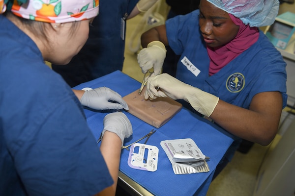 260610-N-JB216-5830 Jacksonville, Fla. (June 12, 2026) The annual Science, Service, Medicine, and Mentoring (S2M2) program at Naval Hospital Jacksonville concluded another impactful week!  From June 8-12, students from Darnell-Cookman School of the Medical Arts explored a variety of medical departments, gaining firsthand experience through hands-on activities, demonstrations, and mentorship from healthcare professionals. The suturing station provided students with hands-on experience in applying stitches, building foundational wound care, and closure techniques. (U.S. Navy photo by Kie Savage).