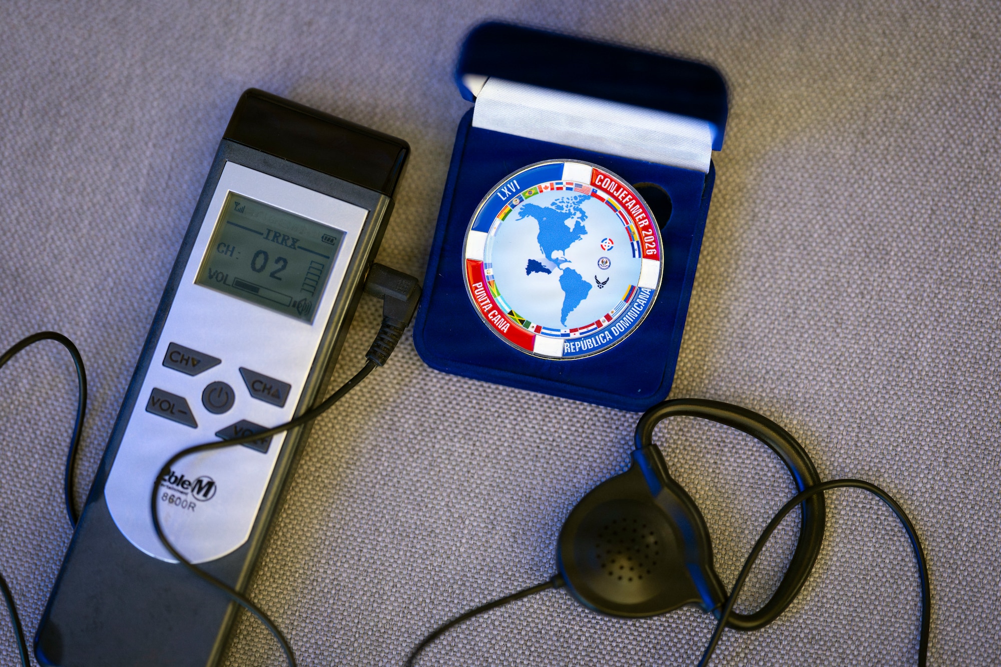 A Conference of the American Air Chiefs (CONJEFAMER) challenge coin rests beside a language interpretation receiver and headset during the 66th annual CONJEFAMER meeting in Punta Cana, Dominican Republic, June 16, 2026. Real-time interpretation services enabled participants from across the Western Hemisphere to receive conference briefings and discussions in their preferred language. (U.S. Air Force photo by Tech. Sgt. Rachel Maxwell)