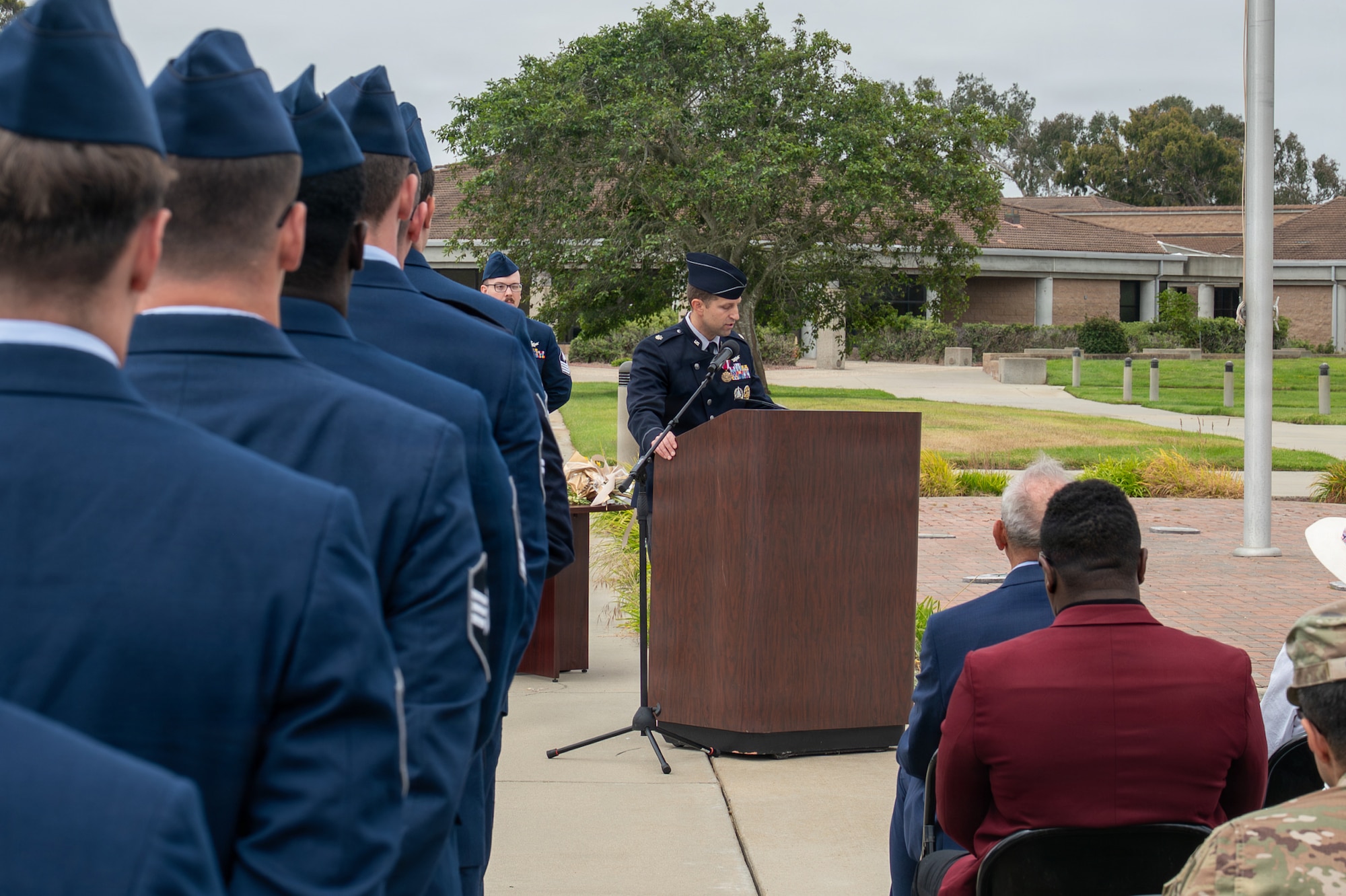 A person stands and speaks behind a podium as people sit and stand listening